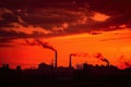 A city skyline with factories and smokestacks silhouetted against a blood-red sunset