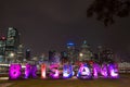 City skyline lights at night beyond bright illuminated city name sign along river walk