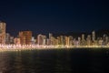 City skyline at night, with the promenades lights twinkling like stars against the dark sea, under a clear sky.