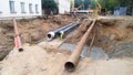 On a city street, a hole was dug to repair and replace sewer and gas pipes. A concrete lining is poured under the pipes. Buildings