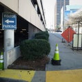 City Urbanscape and Sidewalk Scene with Visitor Parking Directional Sign, Parking Garage and Traffic Cone. Royalty Free Stock Photo