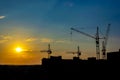 cityscape at sunset with the sun setting behind a building and construction cranes silhouetted against the sky Royalty Free Stock Photo