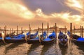 Cityscape with venice blue gondolas on st. mark`s square docks and cloudly sunset on St. Giorgio island with warm colors in backgr