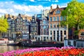 Cityscape view of the canal of Amsterdam in summer with a blue sky, houseboat and traditional old houses. Colorful spring tulips Royalty Free Stock Photo