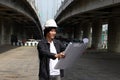 Civil engineer man with helmet, standing and looks at the project drafts while on parallel expressway background