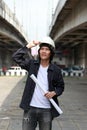 Civil engineer man standing and catch the helmet with project drafts while in hand on parallel expressway background