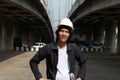 Civil engineer man with white helmet, standing with project drafts in hand and akimbo on parallel expressway background