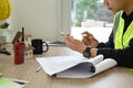 Civil engineer wearing vest working with blueprints and using smart phone at working desk Royalty Free Stock Photo