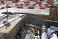 Civil engineering building site with thick pipes covered by layer of insulation foam, secured by red and white barrier planks