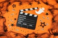 Clapper board in spider webs, spiders, ghost, eyes on orange background.