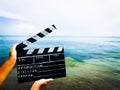 a clapperboard for filmer production in the hands of a man against the background of a sandy beach and the sea.