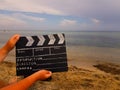 a clapperboard for filmer production in the hands of a man against the background of a sandy beach and the sea.