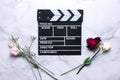 Clapperboard and fresh roses on marble table. Love is just acting concept.