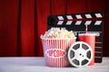 Clapperboard, reel and popcorn bucket on table against stage curtain, space for text. Royalty Free Stock Photo