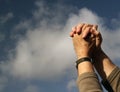 Clasped hands praying. Clouds and sky background.