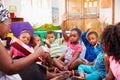 Class of preschool children raising hands to answer teacher