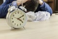 Classic alarm clock on the office table. In the background, the manager buried his head in the crumpled papers and covered it with