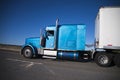 Classic American model big rig semi truck in blue with semi trailer driving on highway on blue sky background Royalty Free Stock Photo