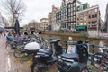 Classic Amsterdam view - bikes, motorbikes and scooters standing by the canal. Outdoor shot. Transportation concept.