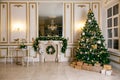 Classic apartments hall with a white fireplace, decorated christmas tree with gift boxes, large mirror and windows