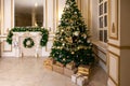 Classic apartments hall with a white fireplace, decorated christmas tree with gift boxes, large mirror and windows