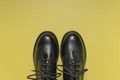 Classic autumn shoes. Fashionable youth black leather boots on yellow background flat lay top view. Stylish womens mens unisex