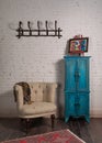 Classic beige armchair, vintage turquoise cupboard, and wall hanger with ornate scarf on bricks wall