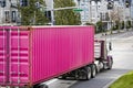 Classic big rig day cab semi truck tractor transporting bright pink container on semi trailer driving on the urban city street Royalty Free Stock Photo