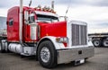 Classic big rig red semi truck tractor with chrome accessories and flat bed semi trailer standing on parking lot waiting for load Royalty Free Stock Photo
