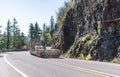 Classic big rig semi truck with empty step down semi trailer turning on the winding road with rock and trees at national Columbia