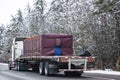 Classic big rig semi truck tractor transporting covered and fastened cargo on flat bed semi trailer driving on the winter highway Royalty Free Stock Photo