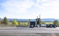 Classic black bonnet big rig semi truck tractor  with vertical chrome pipes running on the road to warehouse for pick up loaded Royalty Free Stock Photo