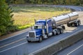 Classic blue bonnet big rig semi truck tractor transporting liquid cargo in tank semi trailer driving on the divided highway with Royalty Free Stock Photo