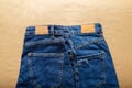 Classic blue jeans. Casual pants clothing blue jeans with brown blank leather labels on beige craft background. Top view