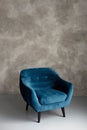 Classic blue velvet art deco armchair with wooden legs against a gray wall. Front view. Soft selective focus Royalty Free Stock Photo