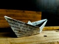 Origami boat crafted from a printed paper, displaying visible text in black ink. The boat is placed on a wooden surface, with a ba Royalty Free Stock Photo