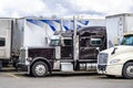 Classic bonnet American dark purple big rig semi truck tractor with loaded dry van semi trailer standing in row with another semi Royalty Free Stock Photo