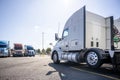 Classic bonnet big rig white semi truck tractor stand on the truck stop parking lot across another semi trucks standing in row for Royalty Free Stock Photo