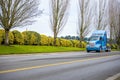 Blue big rig American model modern semi truck tractor driving on the road with trees row on the side