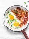 Classic Breakfast - fried eggs and bacon in a cast iron pan on a light background