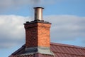 classic brick chimney with metal smoke deflector and stovepipe on a roof with wooden shingles
