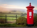 Classic British Red Post Box with a misty countryside backdrop Royalty Free Stock Photo