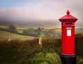 Classic British Red Post Box with a misty countryside backdrop Royalty Free Stock Photo