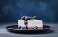 A classic cheesecake slice topped with fresh blueberries on a dark plate over blue background with copy space