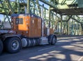 Classic commercial transportation brown big rig semi truck transporting cargo on flat bed semi trailer running on the truss Royalty Free Stock Photo