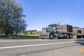 Classic compact powerful old style green big rig semi truck transporting fastened cargo on flat bed semi trailer running on the