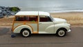 Classic Cream Coloured Morris 1000 Traveller car parked on seafront promenade beach and sea in the background.