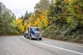 Classic dark blue big rig semi truck transporting stacked cargo on flat bed semi trailer driving on the curved road through the Royalty Free Stock Photo