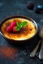 A classic dessert, creme brulee, elegantly presented with a topping of fresh raspberry, on a dark concrete background