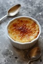 A classic dessert, creme brulee, in a white ramekin, on a grey concrete background